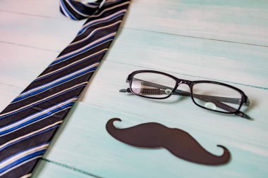 Babalar günün kutlu olsun. Siyah bir bıyık kağıdı, mavi bir kravat ve tahta masada gözlük..