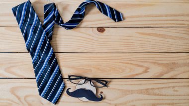 Babalar günün kutlu olsun. Siyah bir bıyık kağıdı, mavi bir kravat ve tahta masada gözlük..