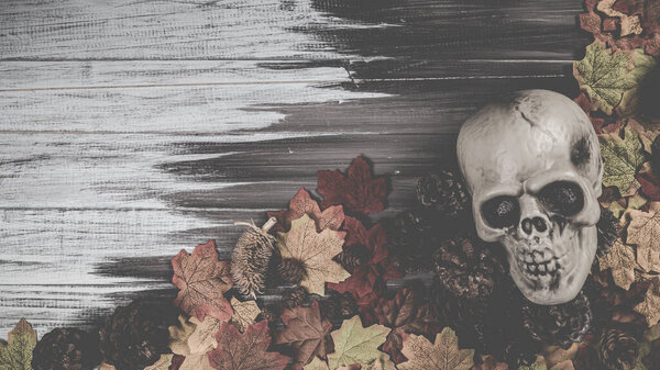 Halloween human skull, Halloween maple leaves on an old wooden table in front of black background with free space for text. Halloween concepts. Happy Halloween Days.