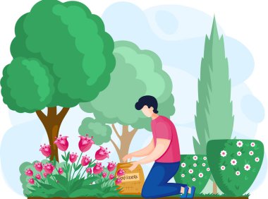 Bahçıvan bahçedeki çiçekleri, ağaçları ve çalıları gübreler. Genç adam toprağı işliyor ve bitki yetiştiriyor.