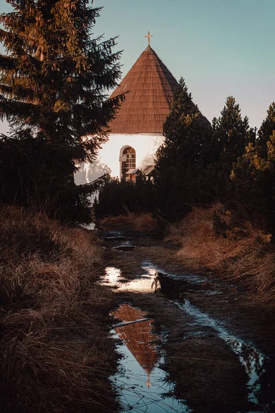 Small chapel with mountain path with puddle at sunset