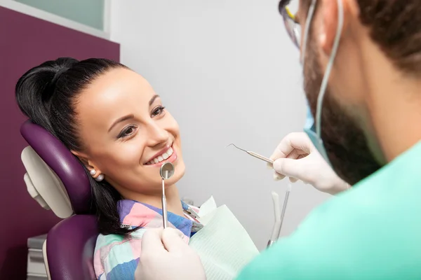 Mujer sentada en silla dental mientras el médico examina sus dientes —  Fotos de Stock