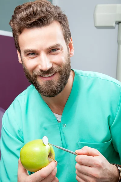 Joven guapo doctor masculino sonriendo con dientes blancos sosteniendo manzana —  Fotos de Stock