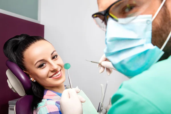 Mulher sentada na cadeira dentária enquanto médico examinando seus dentes — Fotografia de Stock