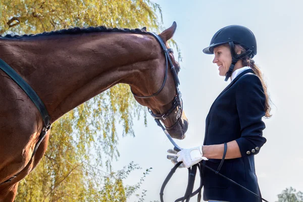 Vackra leende jockey girl stå bredvid sin häst. — Stockfoto