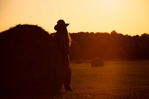 Schönes Mädchen, das neben einem Heuballen auf einem Feld steht. — Stockfoto