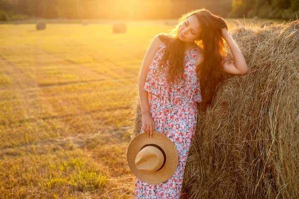 Belle femme debout près d'une balle de foin dans le champ . — Photo