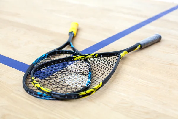 Yellow and blue tennis rackets are lying on wooden court — Stock Photo, Image