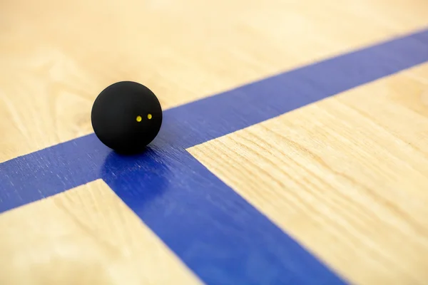 Black tennis ball is lying on wooden court — Stock Photo, Image