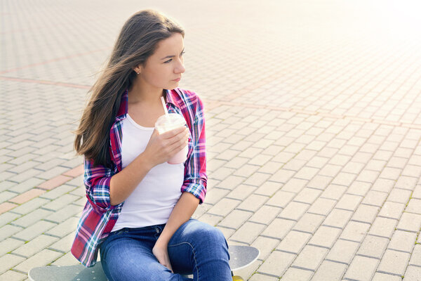 Beautiful young woman with a skateboard and milkshake