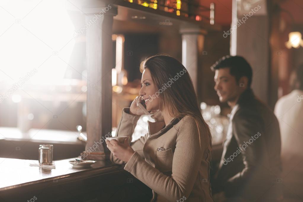 Smiling woman at the bar having a phone call