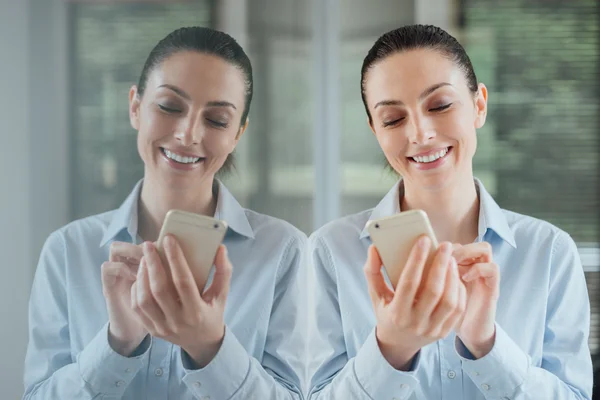 Mulher usando um smartphone e inclinando-se em uma janela — Fotografia de Stock