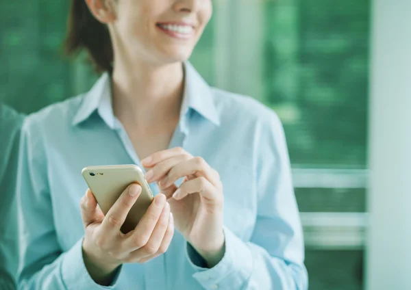 Woman using a smartphone and leaning on a window — Stock Photo, Image