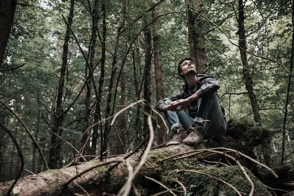 Jonge man zit op een boomstam in het bos — Stockfoto