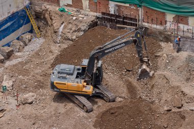 Sarı bir kazıcı, gücünü ve hassasiyetini kullanarak yüksek bir yapının gelecekteki temelini kazıyor. Gücün, ilerlemenin ve her büyük yapının arkasındaki enerjinin sembolü..