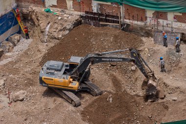 Sarı bir kazıcı, gücünü ve hassasiyetini kullanarak yüksek bir yapının gelecekteki temelini kazıyor. Gücün, ilerlemenin ve her büyük yapının arkasındaki enerjinin sembolü..
