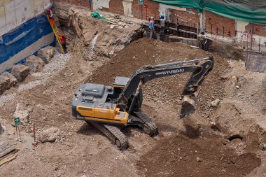 Sarı bir kazıcı, gücünü ve hassasiyetini kullanarak yüksek bir yapının gelecekteki temelini kazıyor. Gücün, ilerlemenin ve her büyük yapının arkasındaki enerjinin sembolü..