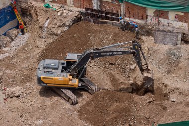 Sarı bir kazıcı, gücünü ve hassasiyetini kullanarak yüksek bir yapının gelecekteki temelini kazıyor. Gücün, ilerlemenin ve her büyük yapının arkasındaki enerjinin sembolü..