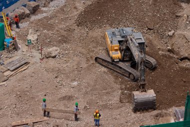 Sarı bir kazıcı, gücünü ve hassasiyetini kullanarak yüksek bir yapının gelecekteki temelini kazıyor. Gücün, ilerlemenin ve her büyük yapının arkasındaki enerjinin sembolü..