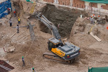 Sarı bir kazıcı, gücünü ve hassasiyetini kullanarak yüksek bir yapının gelecekteki temelini kazıyor. Gücün, ilerlemenin ve her büyük yapının arkasındaki enerjinin sembolü..