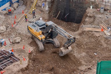 Sarı bir kazıcı, gücünü ve hassasiyetini kullanarak yüksek bir yapının gelecekteki temelini kazıyor. Gücün, ilerlemenin ve her büyük yapının arkasındaki enerjinin sembolü..