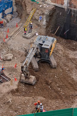 Sarı bir kazıcı, gücünü ve hassasiyetini kullanarak yüksek bir yapının gelecekteki temelini kazıyor. Gücün, ilerlemenin ve her büyük yapının arkasındaki enerjinin sembolü..