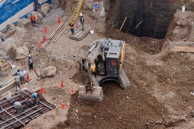 Sarı bir kazıcı, gücünü ve hassasiyetini kullanarak yüksek bir yapının gelecekteki temelini kazıyor. Gücün, ilerlemenin ve her büyük yapının arkasındaki enerjinin sembolü..