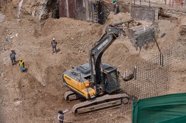 Sarı bir kazıcı, gücünü ve hassasiyetini kullanarak yüksek bir yapının gelecekteki temelini kazıyor. Gücün, ilerlemenin ve her büyük yapının arkasındaki enerjinin sembolü..