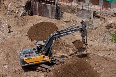 Sarı bir kazıcı, gücünü ve hassasiyetini kullanarak yüksek bir yapının gelecekteki temelini kazıyor. Gücün, ilerlemenin ve her büyük yapının arkasındaki enerjinin sembolü..