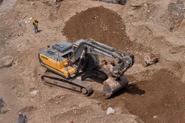 Sarı bir kazıcı, gücünü ve hassasiyetini kullanarak yüksek bir yapının gelecekteki temelini kazıyor. Gücün, ilerlemenin ve her büyük yapının arkasındaki enerjinin sembolü..