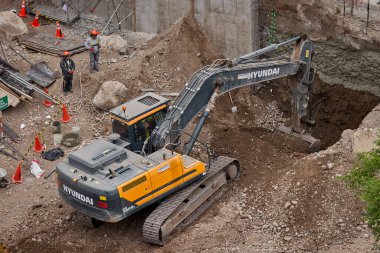 Sarı bir kazıcı, gücünü ve hassasiyetini kullanarak yüksek bir yapının gelecekteki temelini kazıyor. Gücün, ilerlemenin ve her büyük yapının arkasındaki enerjinin sembolü..