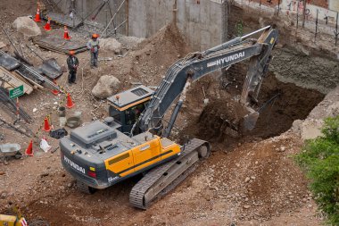 Sarı bir kazıcı, gücünü ve hassasiyetini kullanarak yüksek bir yapının gelecekteki temelini kazıyor. Gücün, ilerlemenin ve her büyük yapının arkasındaki enerjinin sembolü..
