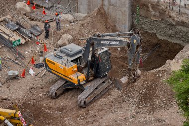 Sarı bir kazıcı, gücünü ve hassasiyetini kullanarak yüksek bir yapının gelecekteki temelini kazıyor. Gücün, ilerlemenin ve her büyük yapının arkasındaki enerjinin sembolü..