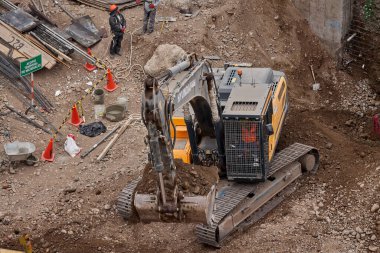 Sarı bir kazıcı, gücünü ve hassasiyetini kullanarak yüksek bir yapının gelecekteki temelini kazıyor. Gücün, ilerlemenin ve her büyük yapının arkasındaki enerjinin sembolü..