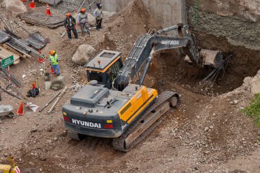 Sarı bir kazıcı, gücünü ve hassasiyetini kullanarak yüksek bir yapının gelecekteki temelini kazıyor. Gücün, ilerlemenin ve her büyük yapının arkasındaki enerjinin sembolü..
