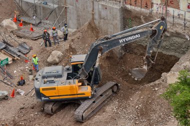Sarı bir kazıcı, gücünü ve hassasiyetini kullanarak yüksek bir yapının gelecekteki temelini kazıyor. Gücün, ilerlemenin ve her büyük yapının arkasındaki enerjinin sembolü..