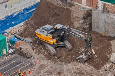 Sarı bir kazıcı, gücünü ve hassasiyetini kullanarak yüksek bir yapının gelecekteki temelini kazıyor. Gücün, ilerlemenin ve her büyük yapının arkasındaki enerjinin sembolü..