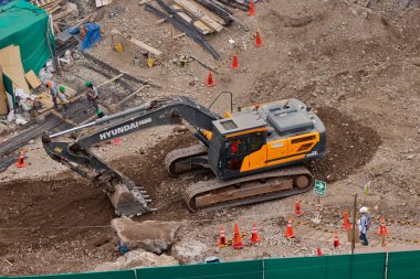 Sarı bir kazıcı, gücünü ve hassasiyetini kullanarak yüksek bir yapının gelecekteki temelini kazıyor. Gücün, ilerlemenin ve her büyük yapının arkasındaki enerjinin sembolü..