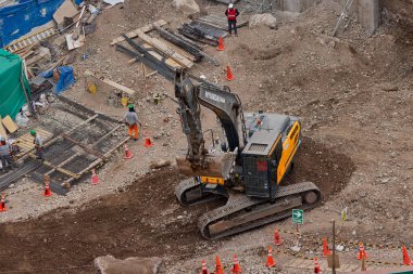 Sarı bir kazıcı, gücünü ve hassasiyetini kullanarak yüksek bir yapının gelecekteki temelini kazıyor. Gücün, ilerlemenin ve her büyük yapının arkasındaki enerjinin sembolü..