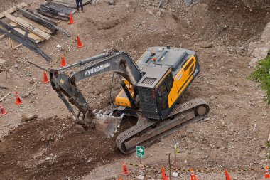 Sarı bir kazıcı, gücünü ve hassasiyetini kullanarak yüksek bir yapının gelecekteki temelini kazıyor. Gücün, ilerlemenin ve her büyük yapının arkasındaki enerjinin sembolü..