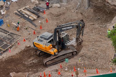 Sarı bir kazıcı, gücünü ve hassasiyetini kullanarak yüksek bir yapının gelecekteki temelini kazıyor. Gücün, ilerlemenin ve her büyük yapının arkasındaki enerjinin sembolü..