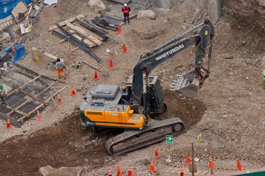 Sarı bir kazıcı, gücünü ve hassasiyetini kullanarak yüksek bir yapının gelecekteki temelini kazıyor. Gücün, ilerlemenin ve her büyük yapının arkasındaki enerjinin sembolü..