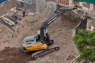 Sarı bir kazıcı, gücünü ve hassasiyetini kullanarak yüksek bir yapının gelecekteki temelini kazıyor. Gücün, ilerlemenin ve her büyük yapının arkasındaki enerjinin sembolü..