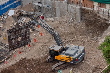 Sarı bir kazıcı, gücünü ve hassasiyetini kullanarak yüksek bir yapının gelecekteki temelini kazıyor. Gücün, ilerlemenin ve her büyük yapının arkasındaki enerjinin sembolü..