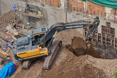 Sarı bir kazıcı, gücünü ve hassasiyetini kullanarak yüksek bir yapının gelecekteki temelini kazıyor. Gücün, ilerlemenin ve her büyük yapının arkasındaki enerjinin sembolü..