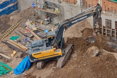 Sarı bir kazıcı, gücünü ve hassasiyetini kullanarak yüksek bir yapının gelecekteki temelini kazıyor. Gücün, ilerlemenin ve her büyük yapının arkasındaki enerjinin sembolü..