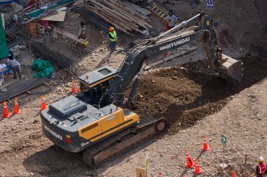 Sarı bir kazıcı, gücünü ve hassasiyetini kullanarak yüksek bir yapının gelecekteki temelini kazıyor. Gücün, ilerlemenin ve her büyük yapının arkasındaki enerjinin sembolü..