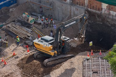 Sarı bir kazıcı, gücünü ve hassasiyetini kullanarak yüksek bir yapının gelecekteki temelini kazıyor. Gücün, ilerlemenin ve her büyük yapının arkasındaki enerjinin sembolü..