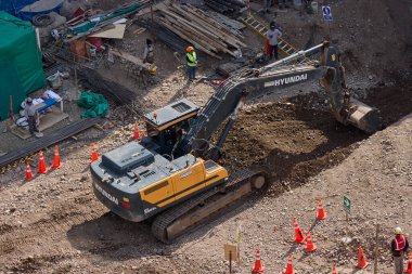 Sarı bir kazıcı, gücünü ve hassasiyetini kullanarak yüksek bir yapının gelecekteki temelini kazıyor. Gücün, ilerlemenin ve her büyük yapının arkasındaki enerjinin sembolü..
