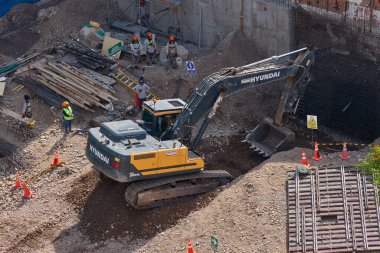 Sarı bir kazıcı, gücünü ve hassasiyetini kullanarak yüksek bir yapının gelecekteki temelini kazıyor. Gücün, ilerlemenin ve her büyük yapının arkasındaki enerjinin sembolü..